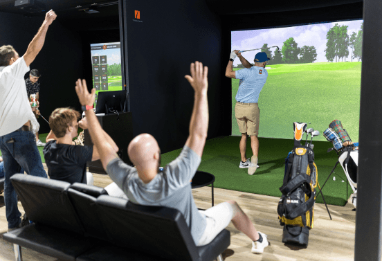 Four men in a simulator bay: one mid-swing, three celebrating behind him