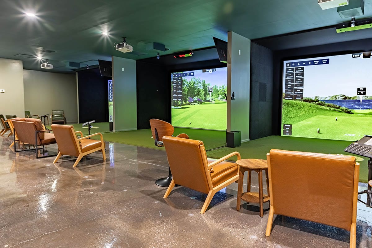 Three simulator bays side by side in a venue lounge, each screen showing the same on-screen data panels